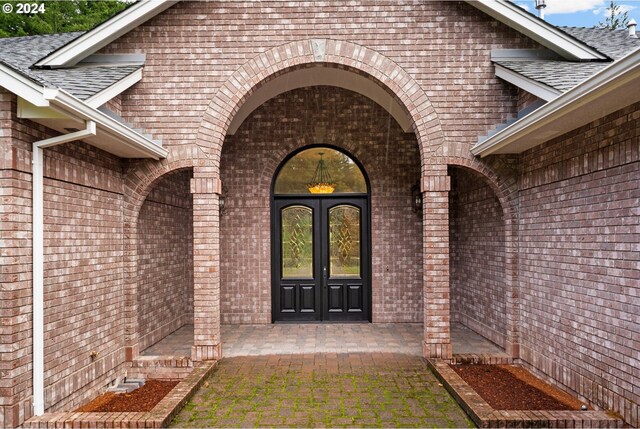 view of exterior entry with french doors, brick siding, and a shingled roof