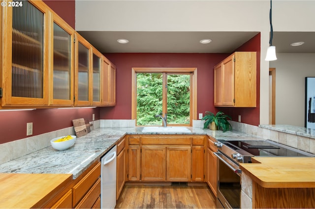 kitchen featuring kitchen peninsula, hanging light fixtures, appliances with stainless steel finishes, light hardwood / wood-style floors, and sink