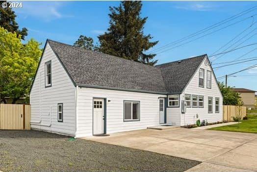 new england style home featuring roof with shingles, a front yard, fence, and a patio