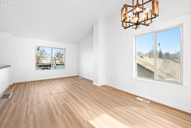 unfurnished living room with vaulted ceiling, light hardwood / wood-style flooring, and a notable chandelier