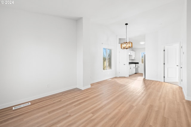 unfurnished living room with a notable chandelier, light wood-type flooring, and vaulted ceiling