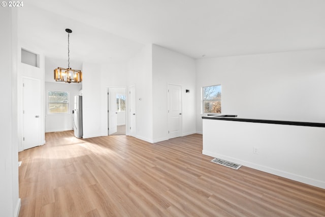 unfurnished living room featuring light hardwood / wood-style floors, a high ceiling, and an inviting chandelier