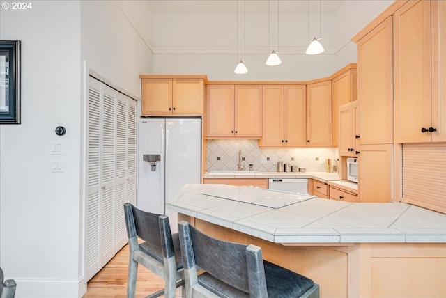 kitchen with light brown cabinetry, light hardwood / wood-style floors, decorative light fixtures, and white appliances