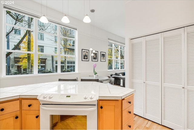 kitchen with tile counters, white range with electric stovetop, and light wood-type flooring