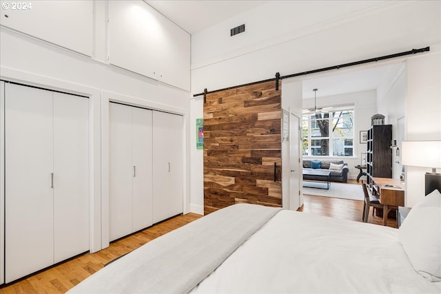 bedroom with wood walls, a barn door, light wood-type flooring, and multiple closets