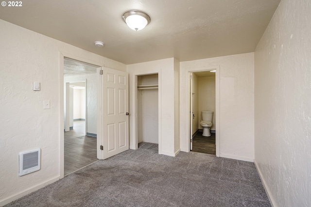 unfurnished bedroom with ensuite bath, a closet, and dark carpet