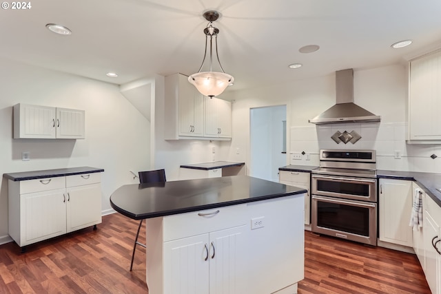 kitchen featuring range with two ovens, a center island, wall chimney exhaust hood, pendant lighting, and white cabinets