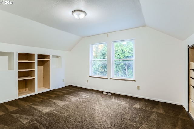 bonus room with a textured ceiling, dark carpet, and vaulted ceiling