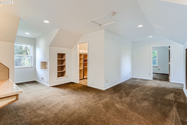 unfurnished living room featuring lofted ceiling, dark colored carpet, and built in shelves