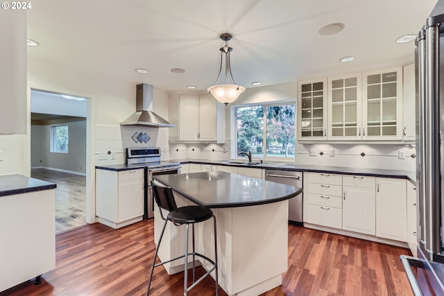 kitchen with wall chimney range hood, appliances with stainless steel finishes, white cabinetry, dark wood-type flooring, and pendant lighting