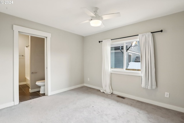 unfurnished bedroom with dark colored carpet, ceiling fan, and ensuite bath