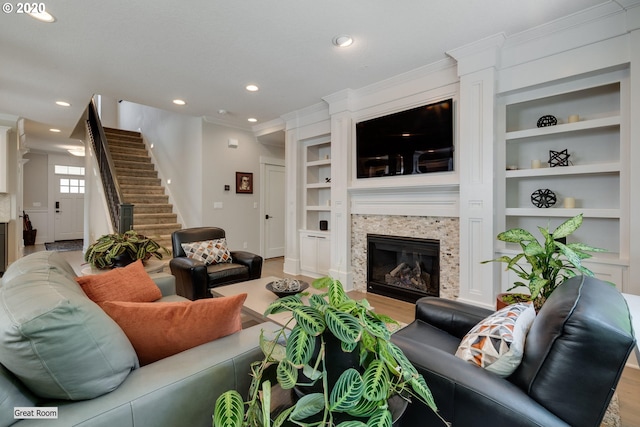 living room with built in shelves, crown molding, a glass covered fireplace, recessed lighting, and stairway