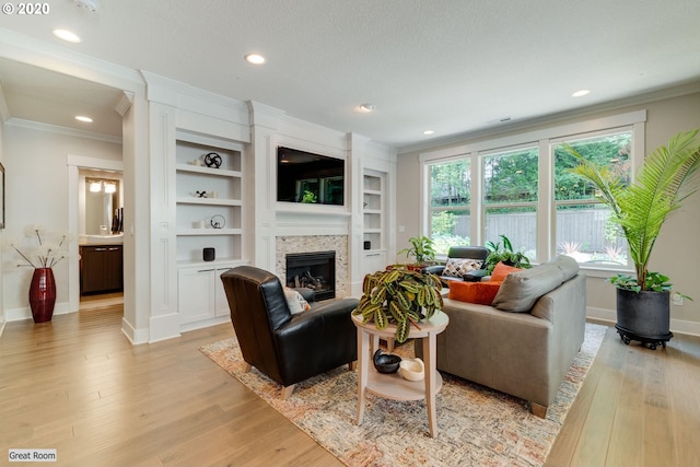living room with crown molding, light wood-style floors, a glass covered fireplace, baseboards, and recessed lighting