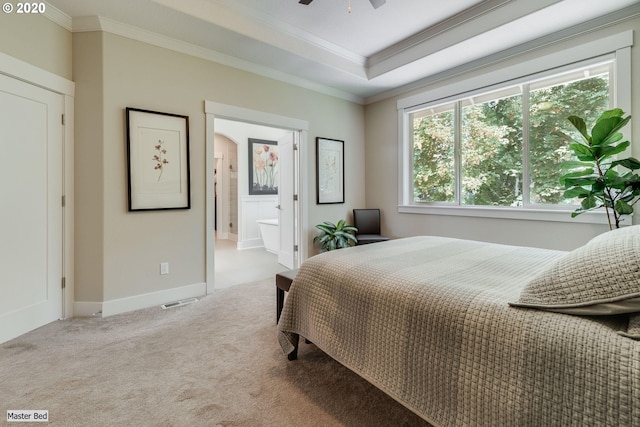 carpeted bedroom with ornamental molding, a raised ceiling, arched walkways, baseboards, and ensuite bathroom
