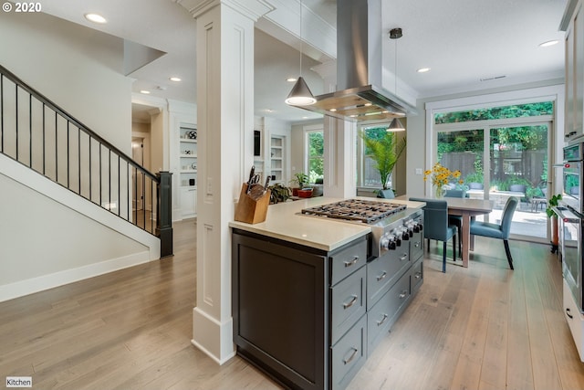 kitchen with island exhaust hood, stainless steel gas stovetop, light countertops, light wood-type flooring, and plenty of natural light