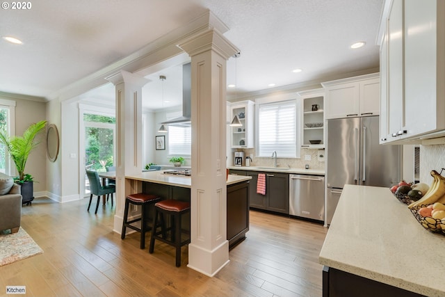 kitchen featuring ornate columns, appliances with stainless steel finishes, a sink, ornamental molding, and healthy amount of natural light