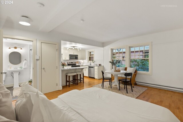 bedroom with sink, baseboard heating, ensuite bathroom, and light hardwood / wood-style flooring