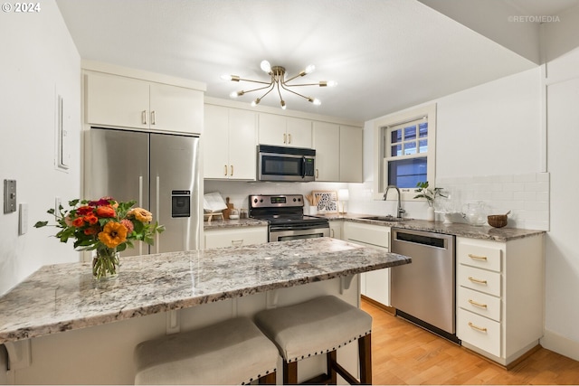 kitchen with a breakfast bar area, light hardwood / wood-style flooring, appliances with stainless steel finishes, decorative backsplash, and white cabinetry