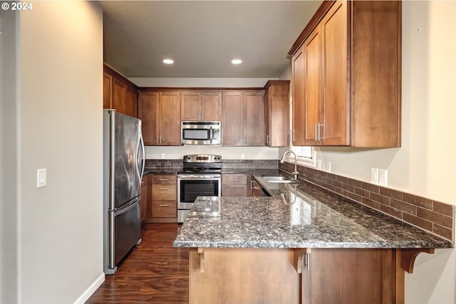 kitchen with a kitchen bar, sink, dark stone countertops, kitchen peninsula, and stainless steel appliances