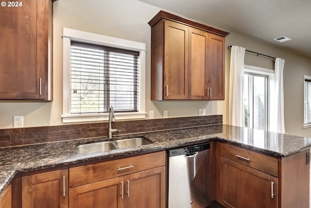 kitchen with a healthy amount of sunlight, dark stone countertops, sink, and stainless steel dishwasher