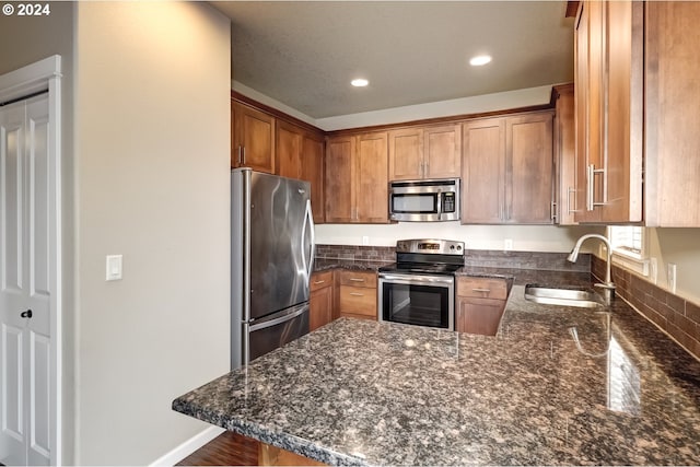 kitchen with stainless steel appliances, sink, dark stone counters, and kitchen peninsula