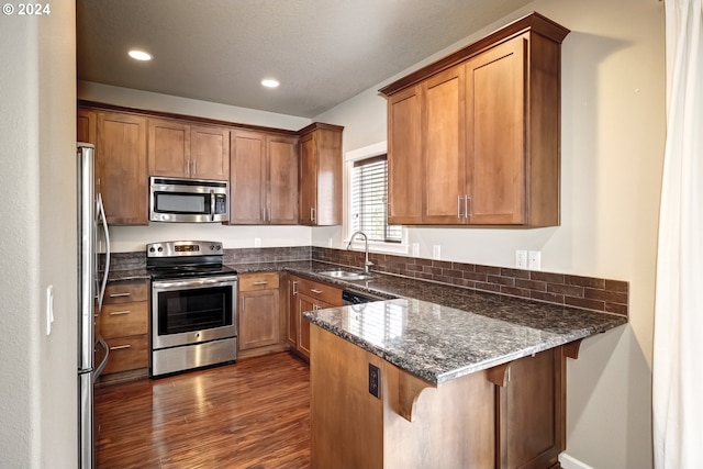 kitchen with sink, stainless steel appliances, a kitchen bar, kitchen peninsula, and dark stone counters