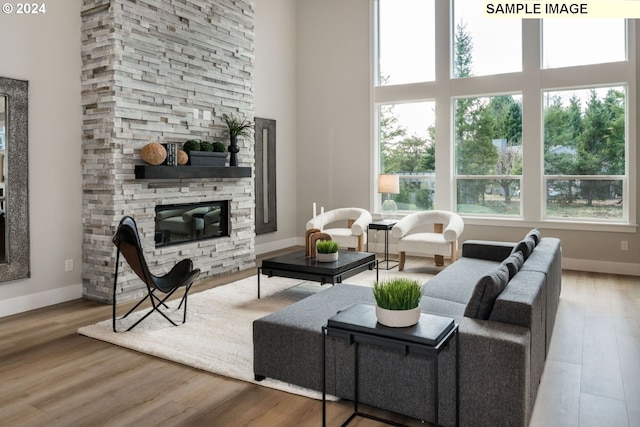 living room with light hardwood / wood-style floors, a stone fireplace, and a towering ceiling