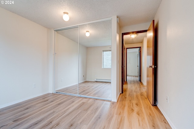 unfurnished bedroom with a textured ceiling, a closet, a baseboard heating unit, and light wood-type flooring