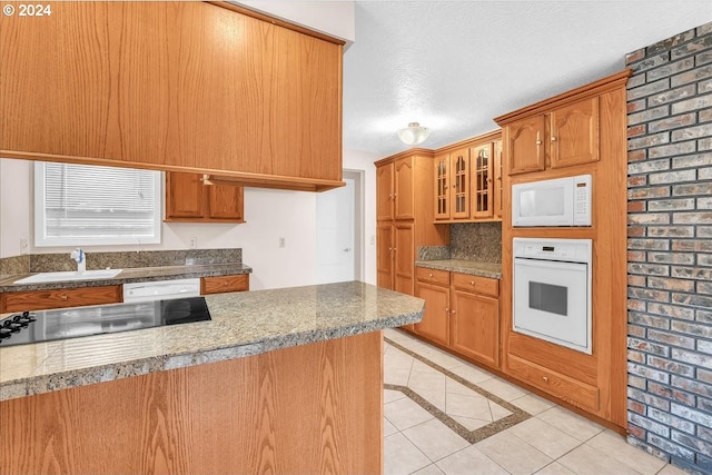 kitchen featuring a textured ceiling, sink, light tile patterned flooring, brick wall, and white appliances