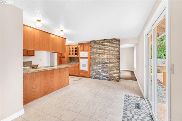 kitchen with kitchen peninsula, white appliances, a textured ceiling, and light tile patterned flooring