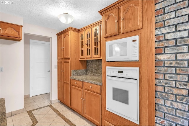 kitchen featuring a textured ceiling, light tile patterned floors, white appliances, and stone counters