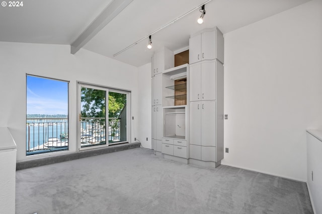 unfurnished bedroom with a water view, carpet floors, vaulted ceiling with beams, and track lighting