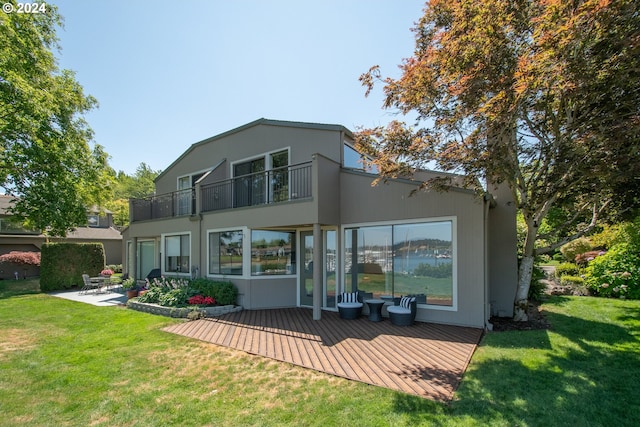 rear view of property with a balcony, a patio area, and a lawn