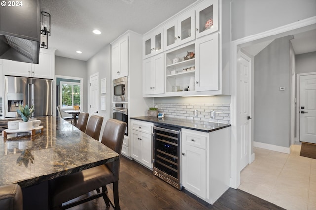 kitchen with appliances with stainless steel finishes, white cabinetry, wine cooler, and dark stone countertops