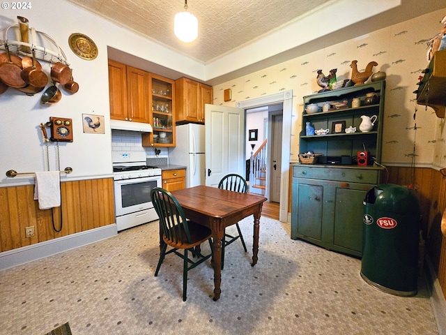 kitchen with a tray ceiling, a textured ceiling, wood walls, decorative backsplash, and white appliances