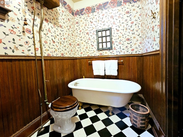 bathroom with wood walls, a washtub, and toilet