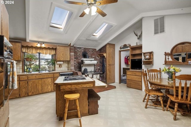 kitchen with ceiling fan, tile counters, sink, kitchen peninsula, and lofted ceiling with skylight