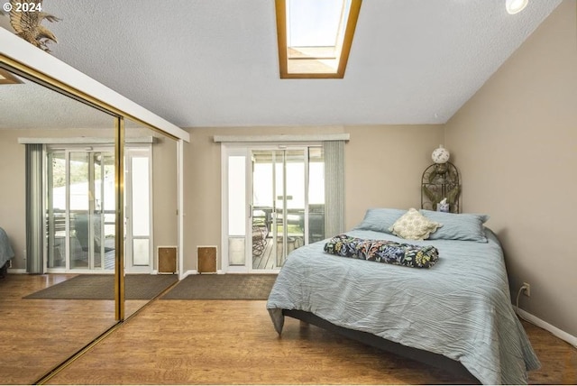 bedroom featuring a skylight, a closet, hardwood / wood-style floors, and access to exterior