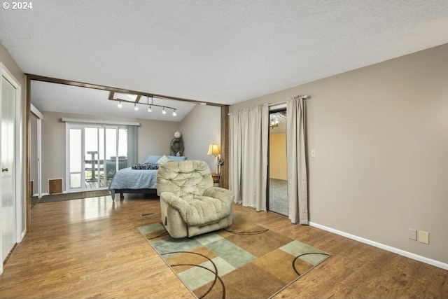 living area with hardwood / wood-style floors, lofted ceiling, a textured ceiling, and track lighting