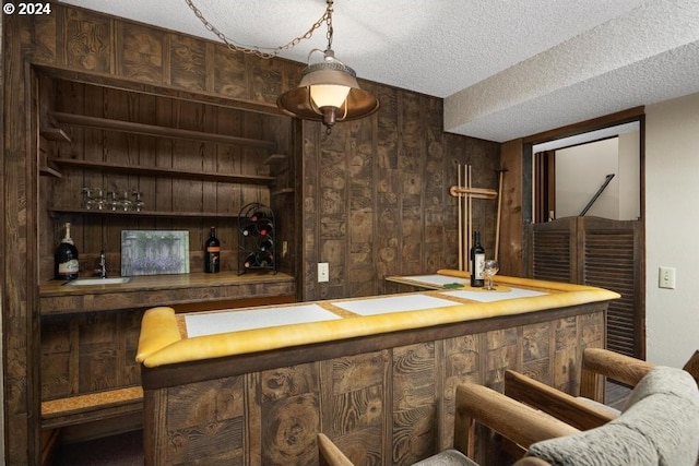 bar featuring wood walls, dark brown cabinetry, and a textured ceiling