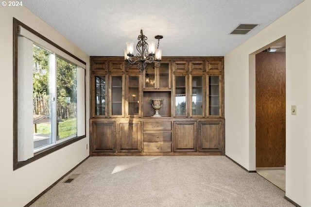 unfurnished dining area with light carpet, a chandelier, and a textured ceiling