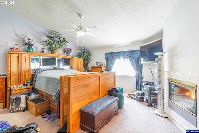 bedroom with ceiling fan, a tile fireplace, a textured ceiling, and light carpet