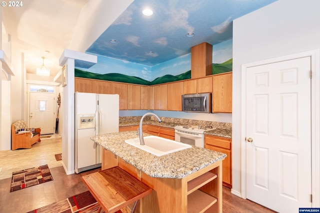 kitchen with a kitchen bar, white appliances, sink, light hardwood / wood-style flooring, and an island with sink