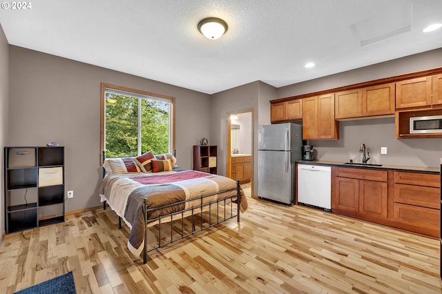 bedroom with connected bathroom, stainless steel refrigerator, sink, a textured ceiling, and light hardwood / wood-style flooring