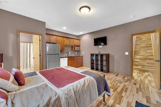 bedroom featuring sink, stainless steel fridge, a textured ceiling, and light hardwood / wood-style flooring