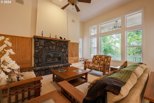 living area with a ceiling fan, visible vents, a stone fireplace, and a towering ceiling