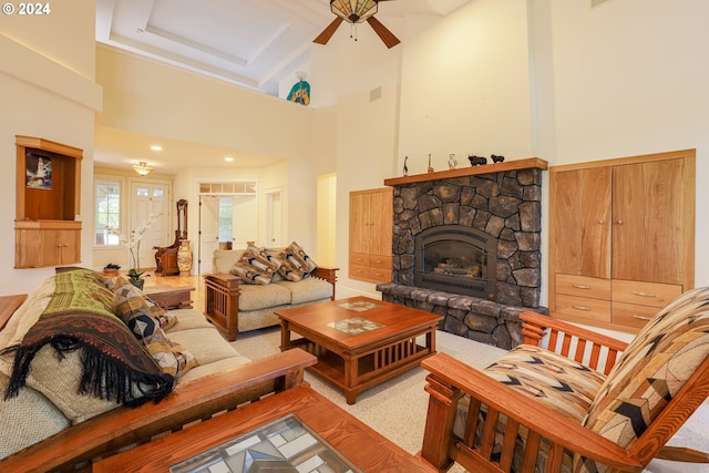 carpeted living room with ceiling fan, a towering ceiling, and a stone fireplace