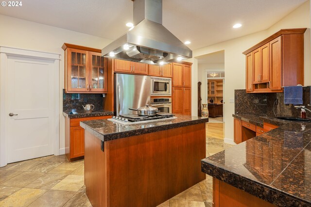 kitchen featuring appliances with stainless steel finishes, light hardwood / wood-style floors, island exhaust hood, a center island, and decorative backsplash