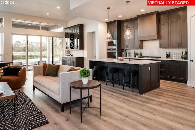 kitchen featuring a breakfast bar, an island with sink, light hardwood / wood-style floors, custom range hood, and stainless steel appliances