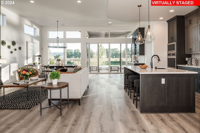 kitchen featuring a kitchen island with sink, hanging light fixtures, stainless steel appliances, and light hardwood / wood-style floors